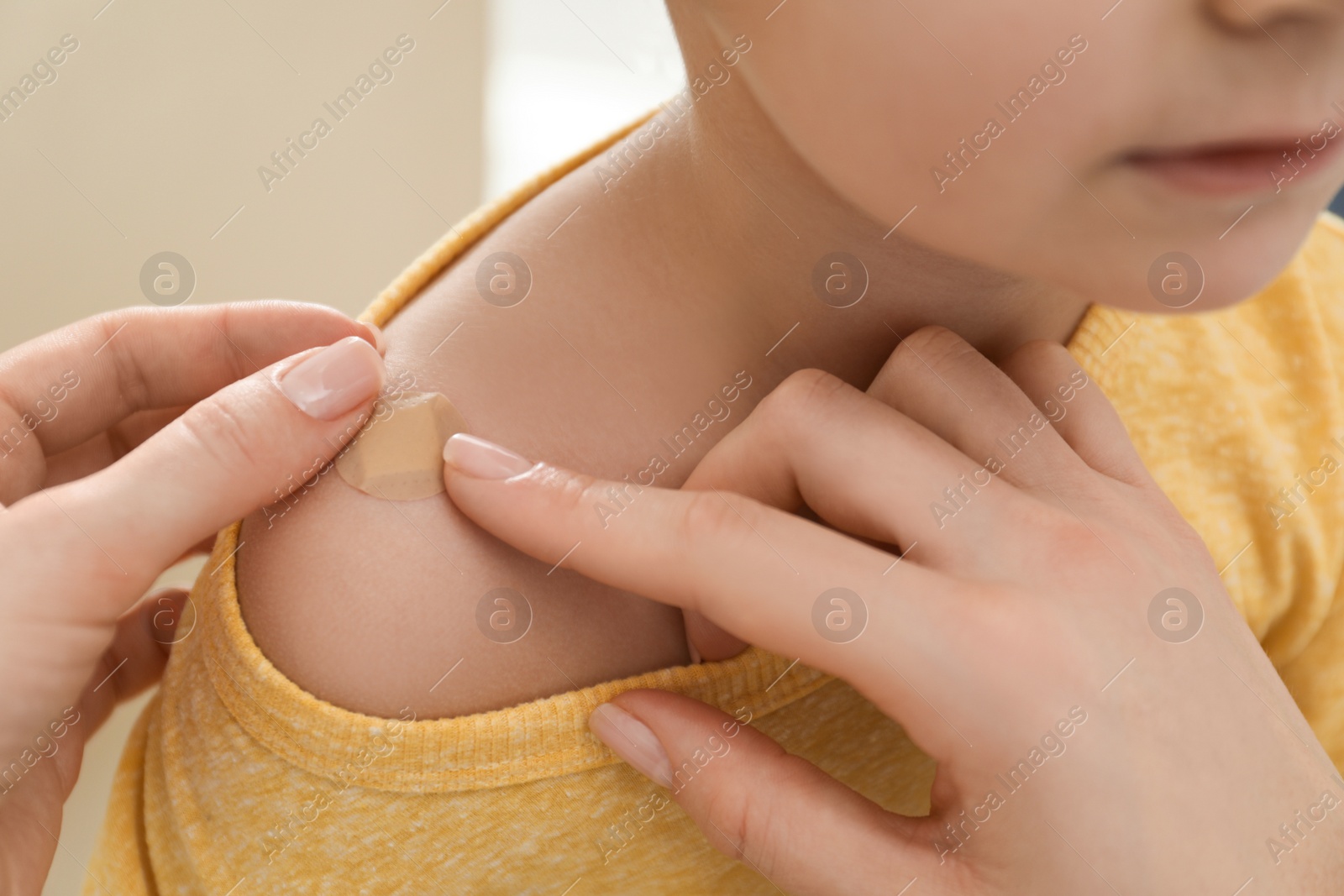 Photo of Mother putting sticking plaster onto son's shoulder indoors, closeup