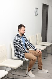Photo of Man sitting on chair and waiting for appointment indoors