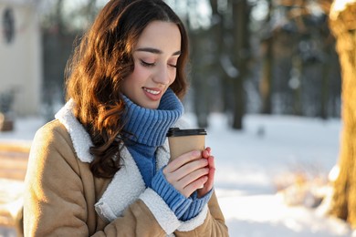 Photo of Portrait of smiling woman with paper cup of coffee in snowy park. Space for text