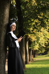 Photo of Young nun reading Bible in park on sunny day. Space for text