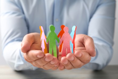 Photo of Man holding paper human figures at table, closeup. Diversity and inclusion concept