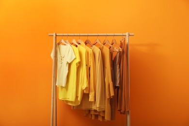 Rack with different stylish women's clothes near orange wall