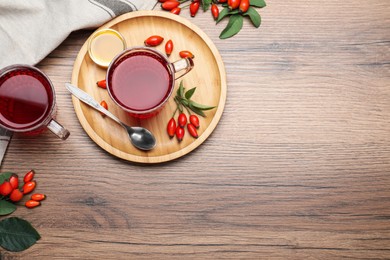 Photo of Fresh rose hip tea, honey and berries on wooden table, flat lay. Space for text