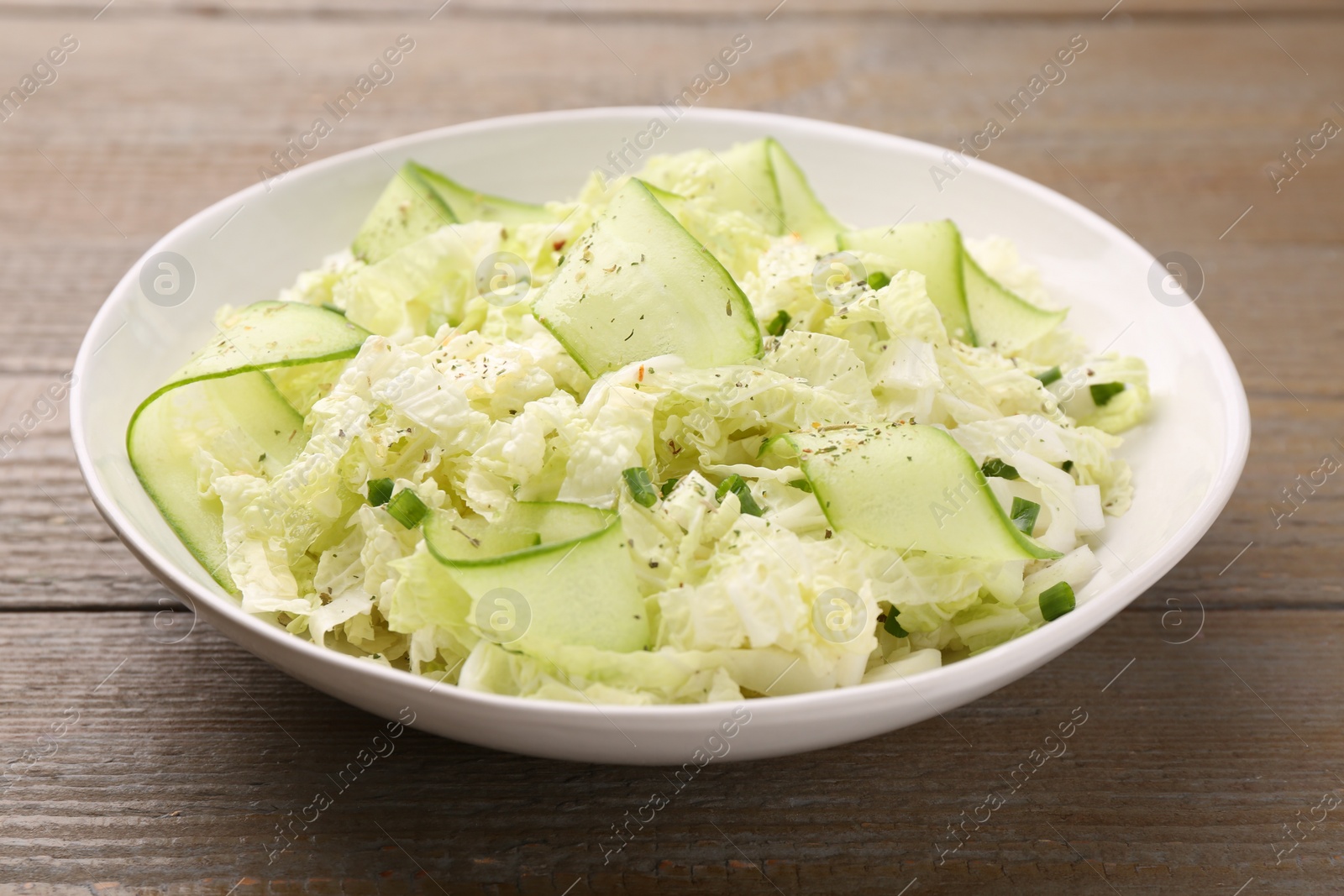 Photo of Tasty salad with Chinese cabbage, cucumber and green onion in bowl on wooden table, closeup