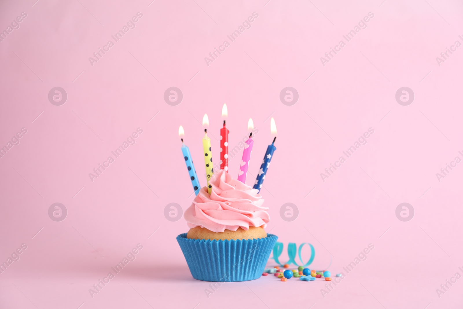 Photo of Delicious birthday cupcake with burning candles, sprinkles and streamer on pink background