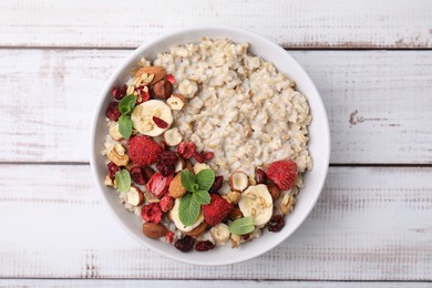 Photo of Delicious oatmeal with freeze dried berries, banana, nuts and mint on white wooden table, top view