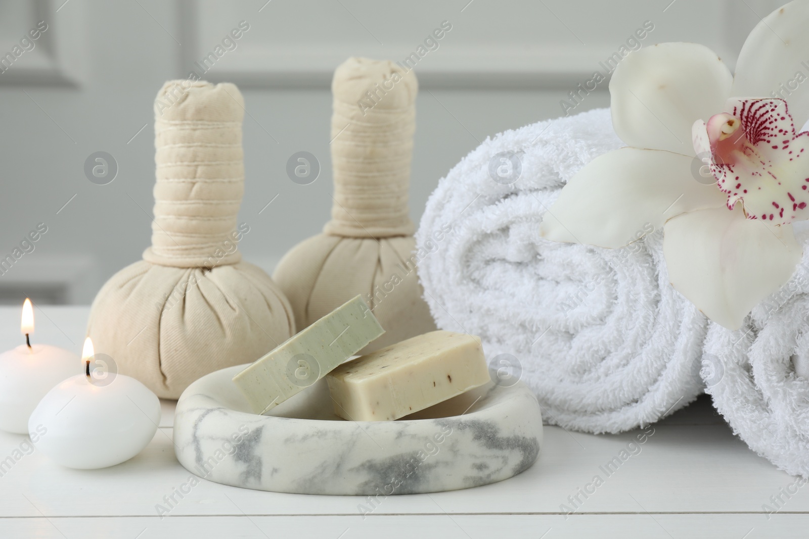 Photo of Beautiful spa composition. Towels, herbal bags, soap bars and burning candles on white wooden table, closeup