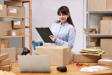 Photo of Parcel packing. Post office worker with clipboard writing notes at wooden table indoors