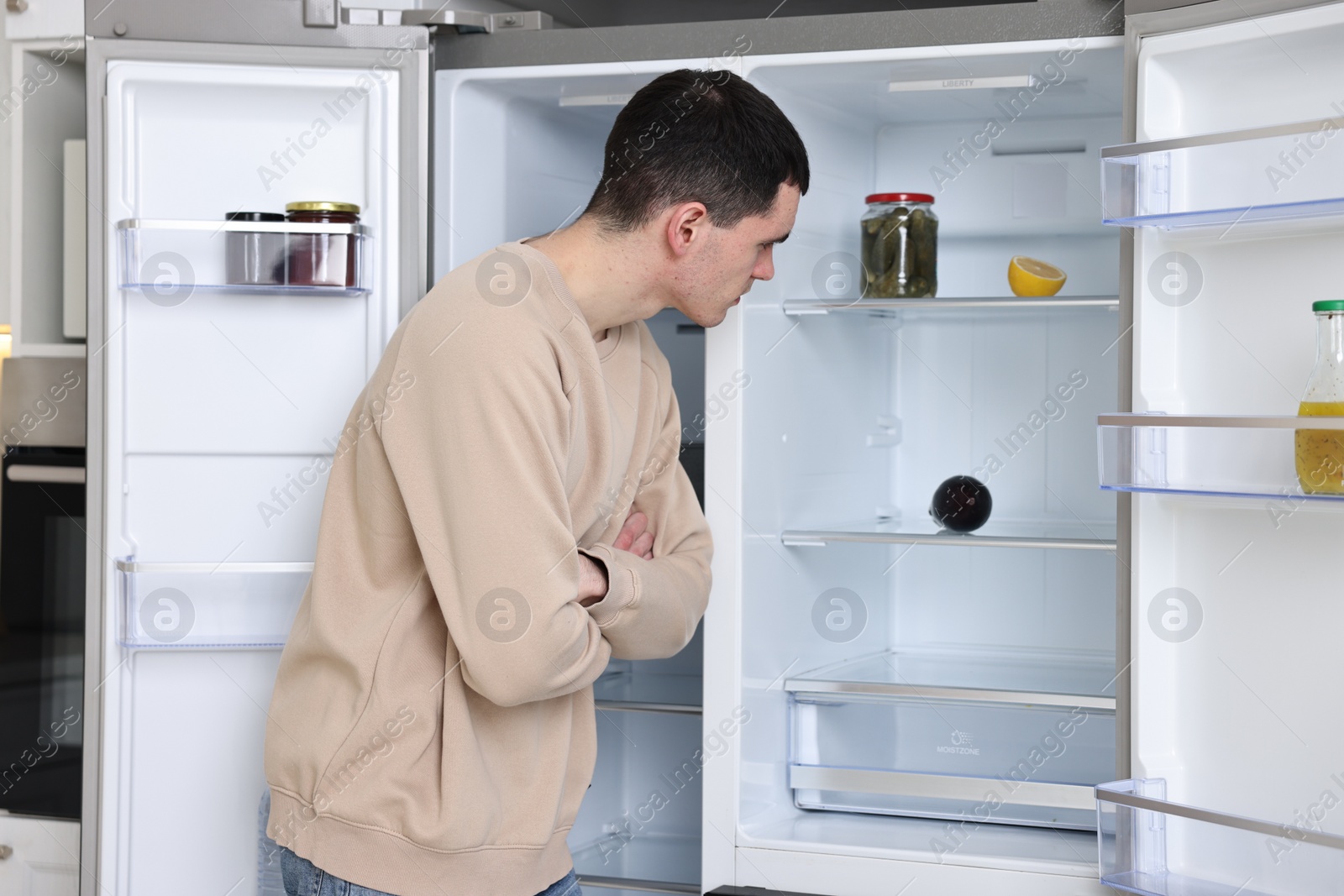 Photo of Thoughtful man near empty refrigerator in kitchen