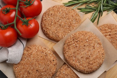 Raw vegan cutlets with breadcrumbs, tomatoes and rosemary on wooden board, above view