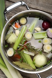 Different ingredients for cooking tasty bouillon in pot and celery on wooden table, flat lay