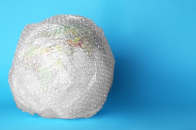 Photo of Globe packed in bubble wrap on turquoise background, space for text. Environmental conservation