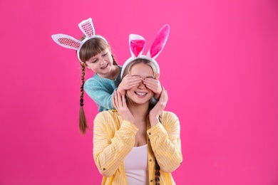 Photo of Happy woman and daughter with bunny ears on color background