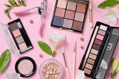 Photo of Flat lay composition with eyeshadow palettes and beautiful flowers on pink background