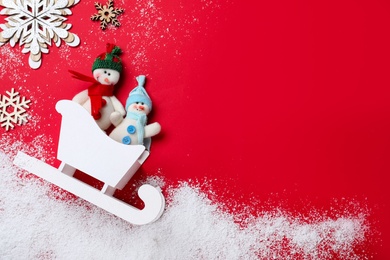 Photo of Flat lay composition with sleigh, toy snowmen and Christmas decorations on red background. Space for text
