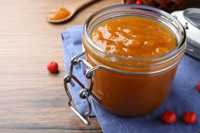 Photo of Delicious rowan jam in glass jar on wooden table. Space for text