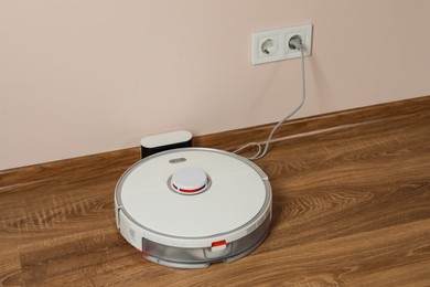 Photo of Robotic vacuum cleaner charging on wooden floor indoors