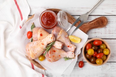 Marinade, raw chicken drumsticks, tomatoes and rosemary on white wooden table, flat lay