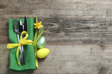 Photo of Cutlery set, painted eggs and beautiful flower on wooden table, flat lay with space for text. Easter celebration