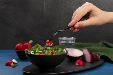 Photo of Woman eating salad with radish at blue wooden table, closeup. Space for text