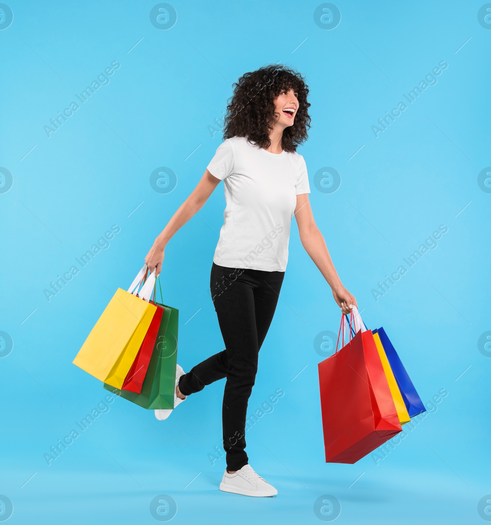 Photo of Happy young woman with shopping bags on light blue background