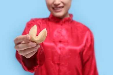 Photo of Young woman holding tasty fortune cookie with prediction on light blue background, closeup