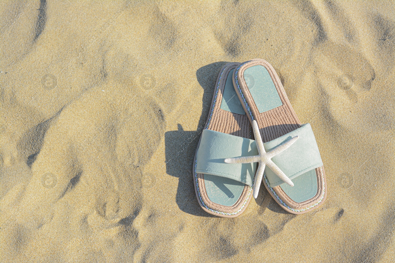 Photo of Stylish slippers and dry starfish on sandy beach, flat lay. Space for text