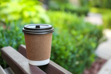 Photo of Disposable paper cup with plastic lid on wooden bench outdoors, space for text