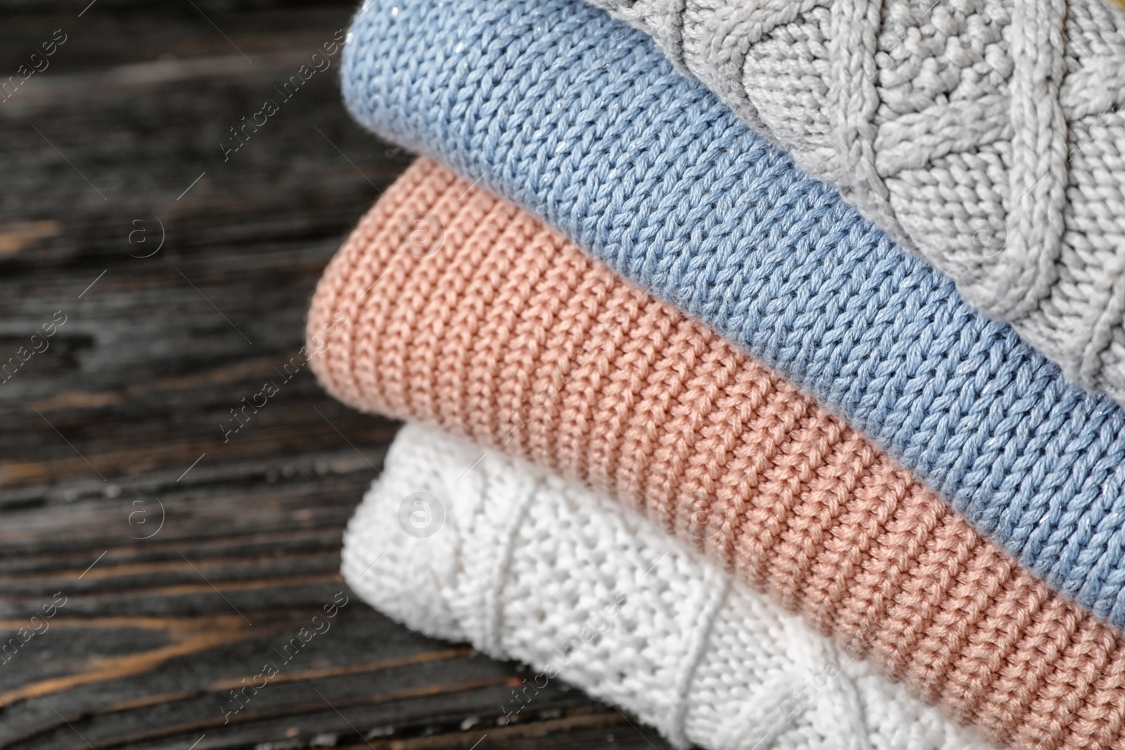 Photo of Stack of folded knitted sweaters on table, closeup