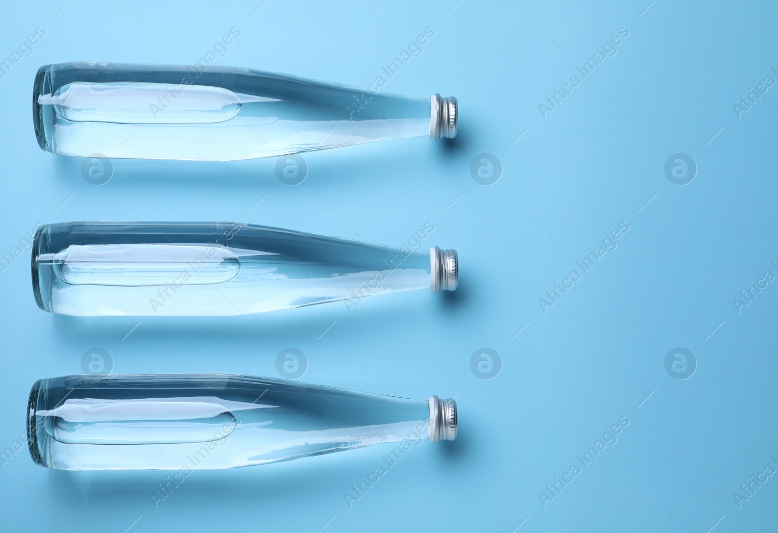 Photo of Glass bottles with water on light blue background, flat lay. Space for text