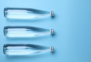 Photo of Glass bottles with water on light blue background, flat lay. Space for text