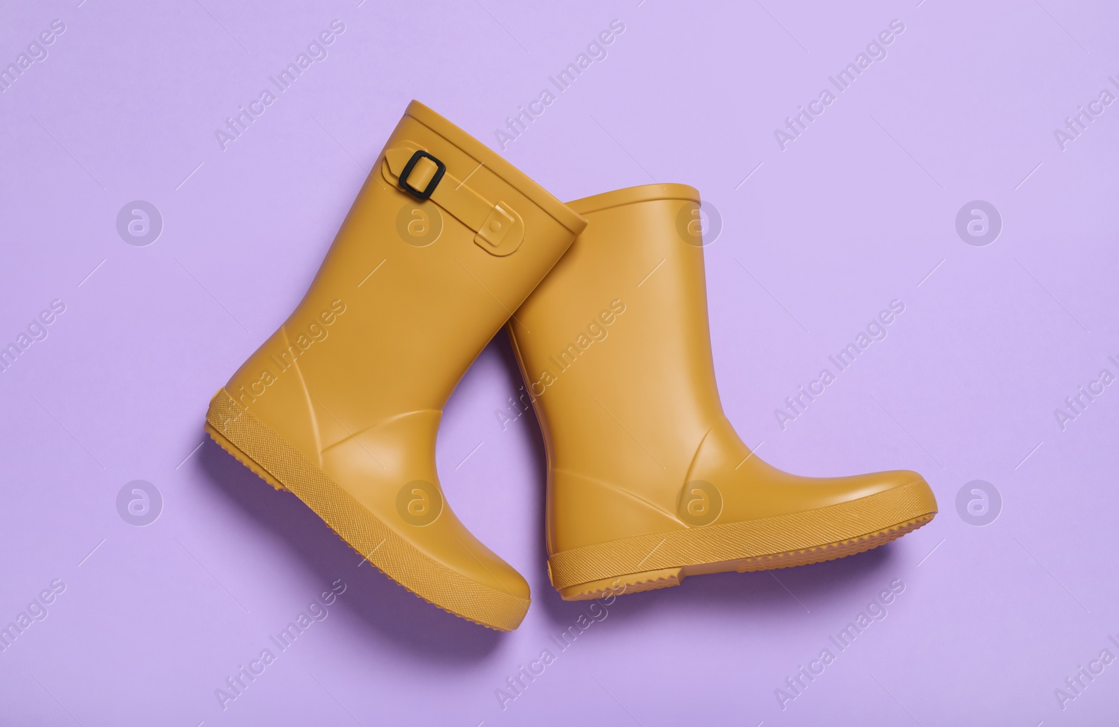 Photo of Pair of yellow rubber boots on violet background, top view