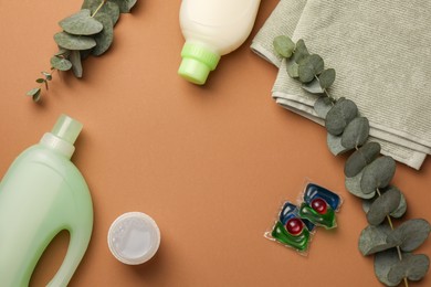 Photo of Flat lay composition with bottles of fabric softener and laundry detergent pods on brown background, space for text