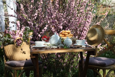 Photo of Beautiful spring flowers, freshly baked waffles and ripe strawberries on table served for tea drinking in garden