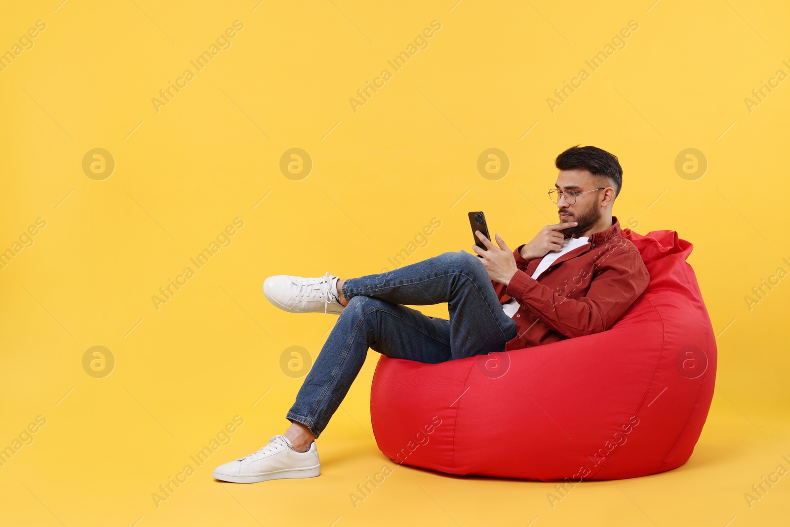 Photo of Handsome young man using smartphone on bean bag chair against yellow background, space for text