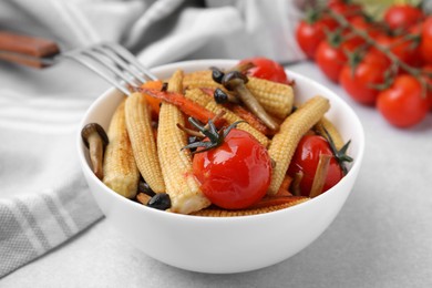 Tasty roasted baby corn with tomatoes and mushrooms on light grey table, closeup