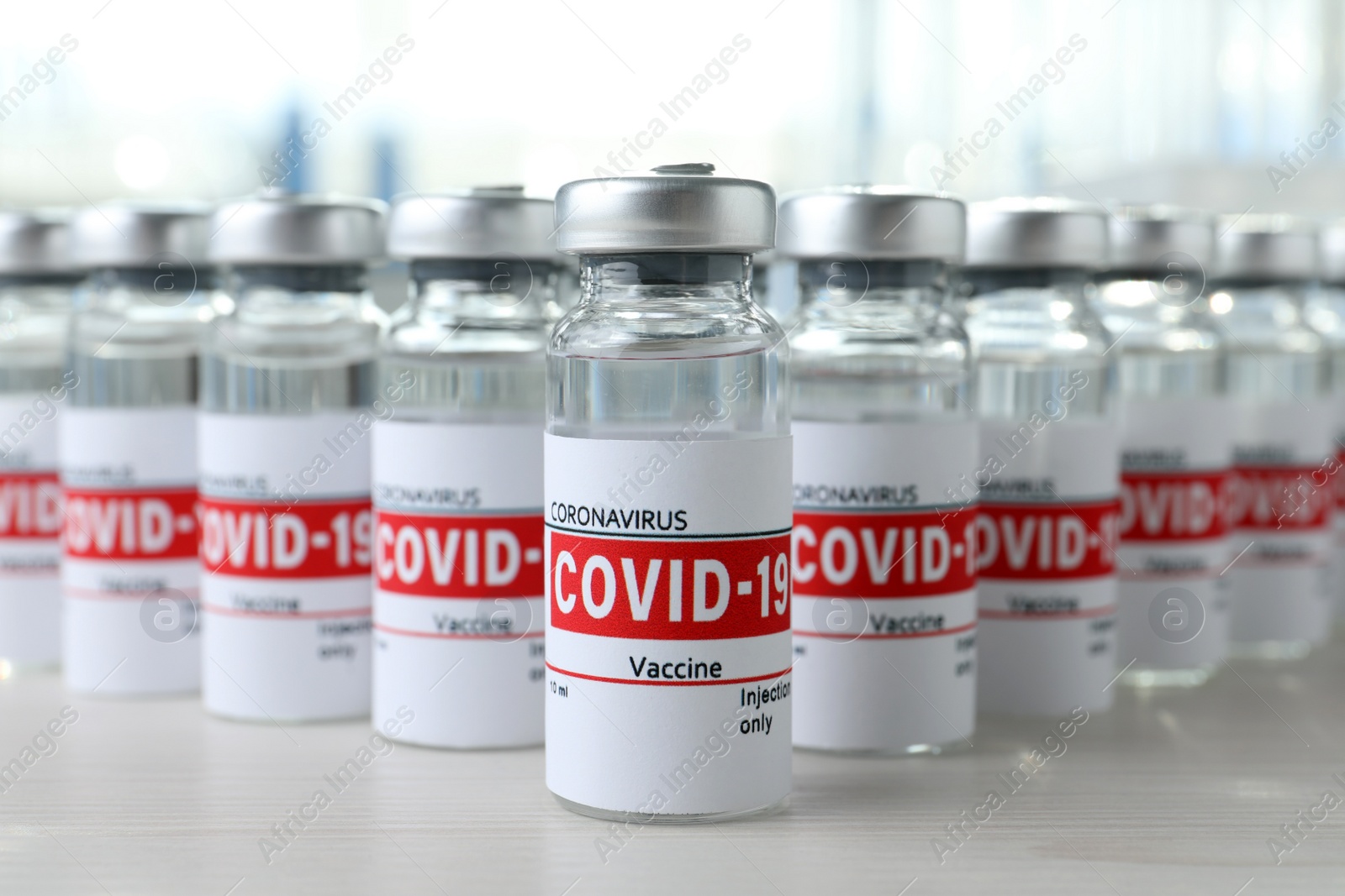 Photo of Glass vials with COVID-19 vaccine on white wooden table