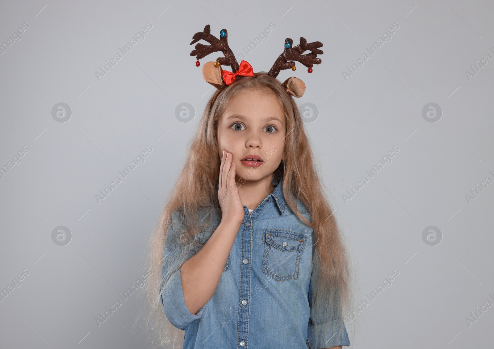 Photo of Excited girl wearing decorative Christmas headband on light grey background