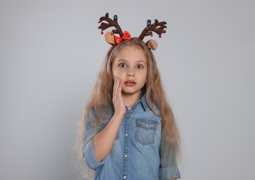 Photo of Excited girl wearing decorative Christmas headband on light grey background