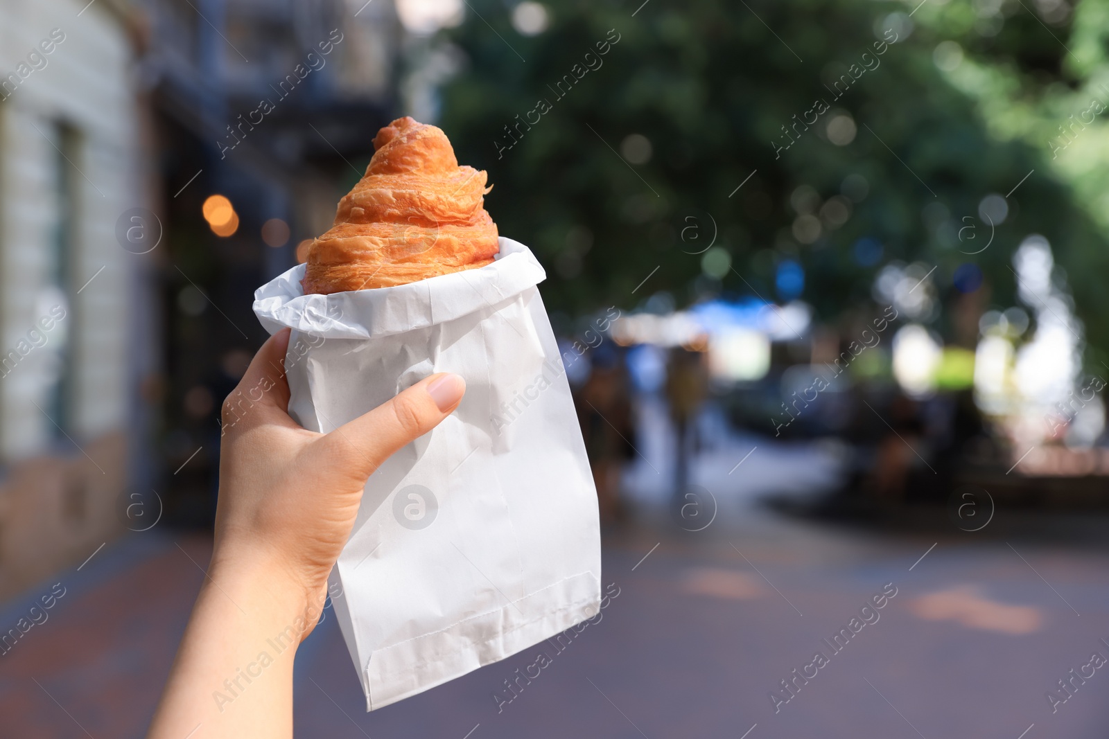 Photo of Woman holding croissant in hand on city street, closeup. Space for text