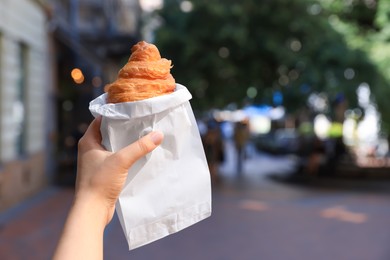 Photo of Woman holding croissant in hand on city street, closeup. Space for text