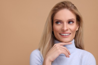Photo of Portrait of smiling middle aged woman with blonde hair on beige background. Space for text