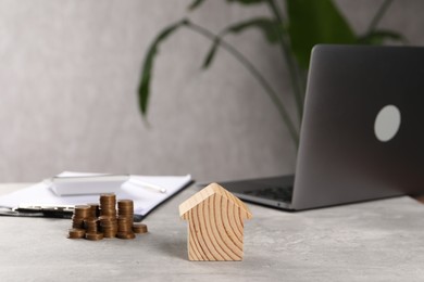 Photo of House model, stacked coins, laptop and clipboard on grey table, selective focus