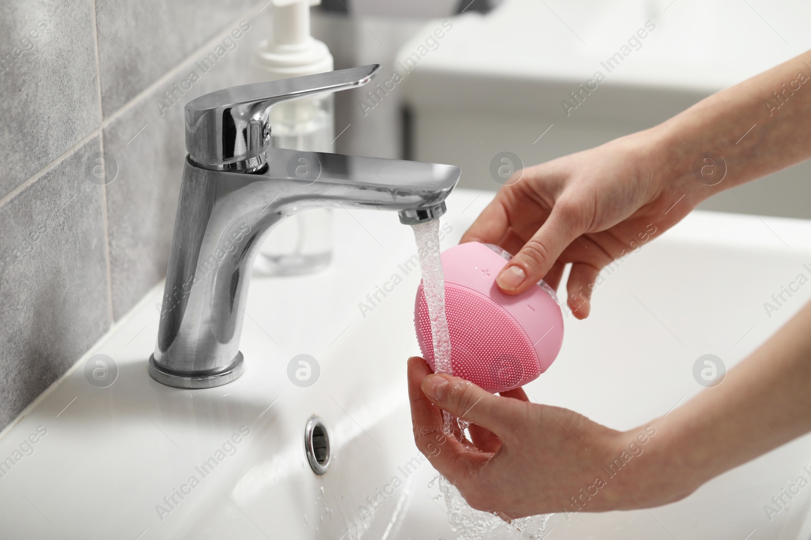 Photo of Young woman washing facial brush in bathroom, closeup