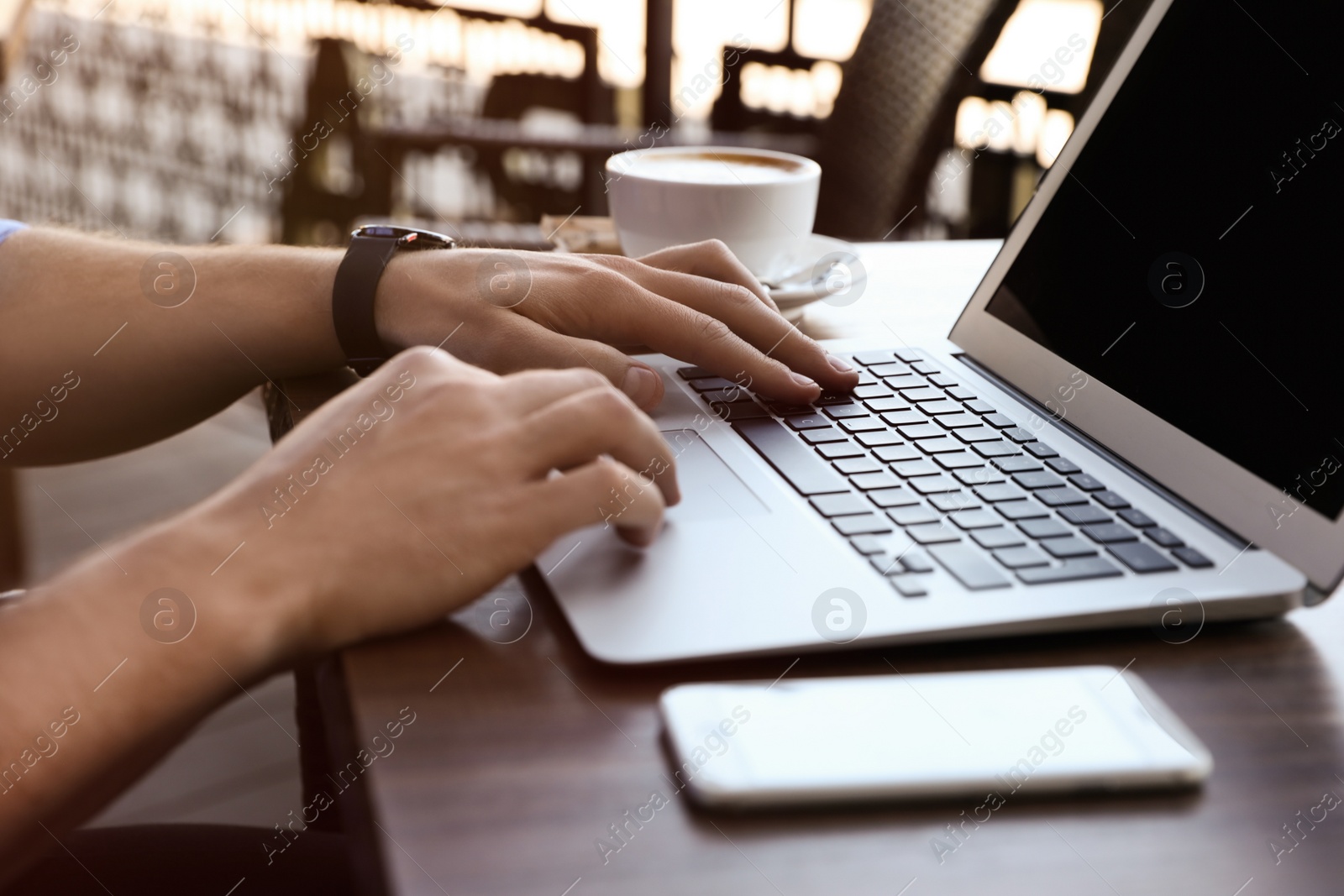 Photo of Young man with laptop sitting at table in cafe outdoors, closeup. Space for text