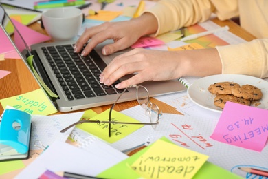 Woman using laptop at messy table, closeup. Concept of being overwhelmed by work