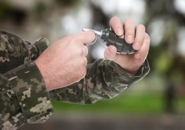 Image of Soldier pulling safety pin out of hand grenade outdoors, closeup