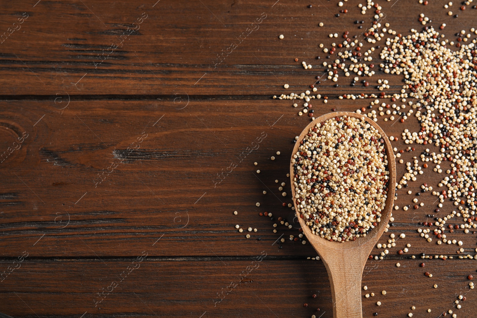 Photo of Spoon with mixed quinoa seeds and space for text on wooden background, top view