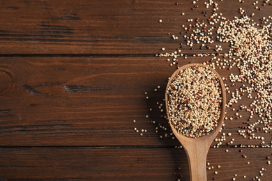 Photo of Spoon with mixed quinoa seeds and space for text on wooden background, top view