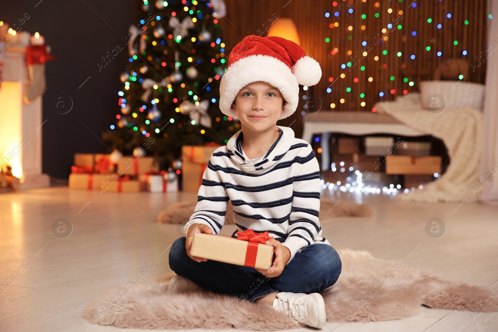 Photo of Cute little child in Santa hat with Christmas gift box at home